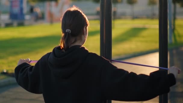Giovane donna sta facendo esercizio fisico con elastico nel parco — Video Stock