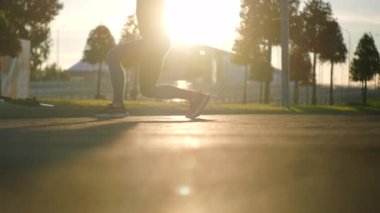 Kadın sporcu ısınıyor ve parka atlıyor.