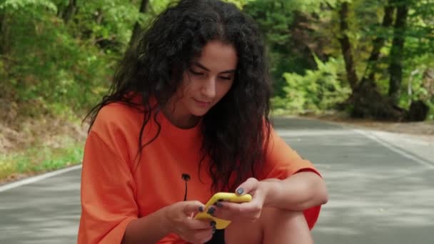 Brunette woman is viewing photos in smartphone outdoors in park — Stock Video