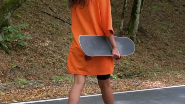 Молодая женщина со скейтбордом в руках идет на улицу, спортивное хобби — стоковое видео