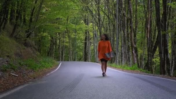 Девушка-скейтбордистка ходит одна в лесу на летних каникулах, везя с собой доску — стоковое видео