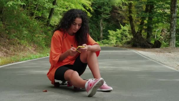 Girl skateboarder chatting dengan teman-teman di ponsel setelah perjalanan — Stok Video