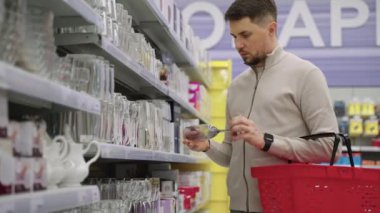 Adam tek başına alışveriş yapıyor, süpermarkette şarap kadehi seçiyor.