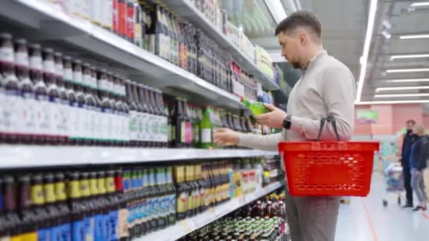 Süpermarkette bira reyonunda alışveriş yapan yetişkin bir adam iki şişe alıyor. — Stok video