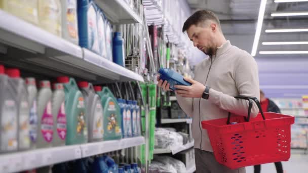 Мужчина водитель выбирает машинное масло в супермаркете, читая этикетку на пластиковой бутылке — стоковое видео