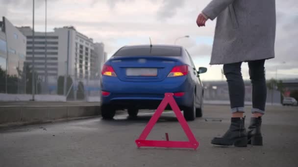 Vrouwelijke bestuurder zet noodwaarschuwing driehoek achter kapotte auto — Stockvideo