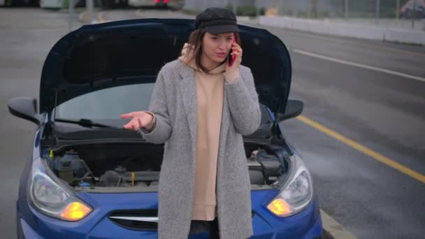 Female driver is calling to car service, standing near broken car at road, call to insurance company — Stock Video