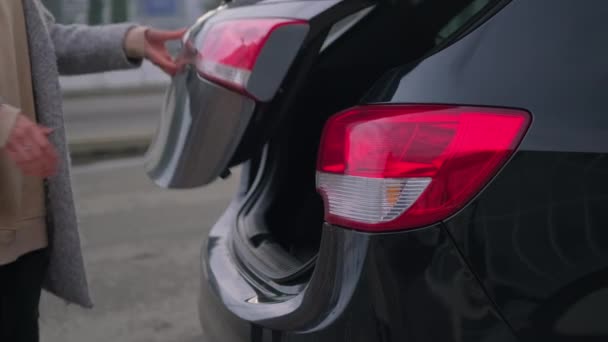 Travelling by car, woman is putting suitcase in trunk of modern automobile, closeup — Stock Video