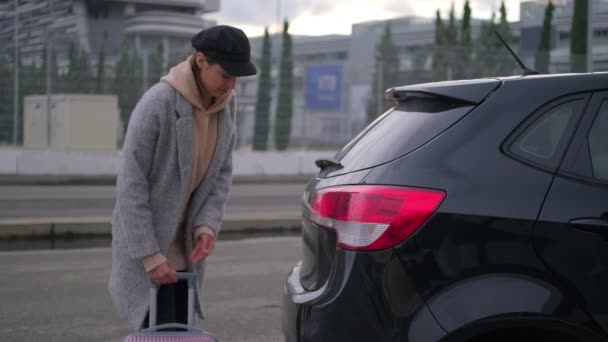 Young woman is opening trunk of her auto and putting suitcase inside — Stock Video