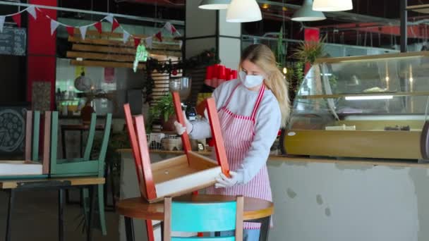 Mitarbeiterin eines kleinen Cafés stellt Stühle auf den Boden, Mundschutz und Handschuhe, Verhinderung der Ausbreitung des Coronavirus — Stockvideo
