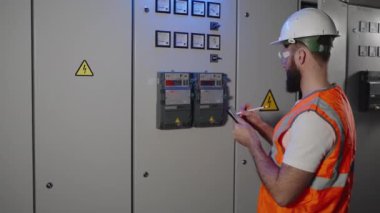 İşçi elektrik panelini ve sayaç ölçümlerini elektronik raporda kontrol ediyor.