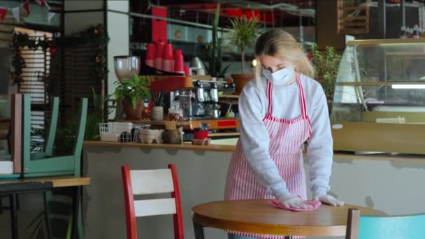 Cameriera sta disinfettando superficie del tavolo in caffè a pandemia di covid-19, indossando maschera e guanti — Video Stock