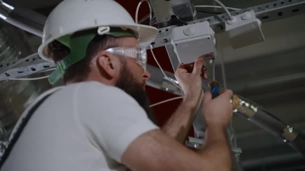 Trabajador está reparando el sistema eléctrico en taller de la planta, instalando caja de conexiones — Vídeo de stock