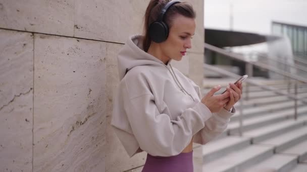 Sportswoman is using modern mobile phone and wireless headphones — Stock Video