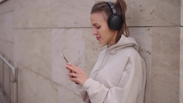 Mladá žena poslouchá píseň z telefonu, pomocí moderních bezdrátových sluchátek — Stock video