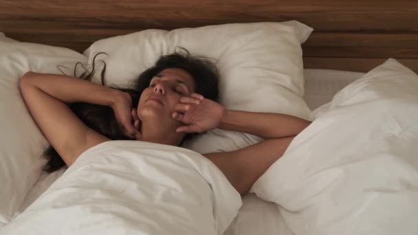 Νεαρή γυναίκα κοιμάται στο δωμάτιό της το ηλιόλουστο πρωί, πετώντας και γυρίζοντας — Αρχείο Βίντεο