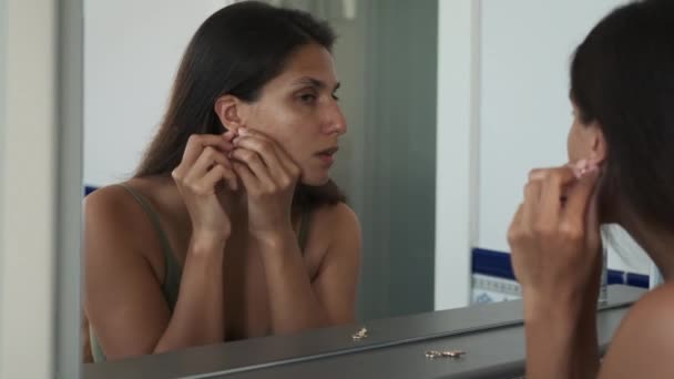 Bella bruna guardando nello specchio e mettendo orecchini in — Video Stock
