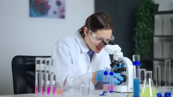 Mujer feliz está viendo virus o bacterias en el microscopio en el laboratorio, haciendo descubrimiento científico — Vídeo de stock