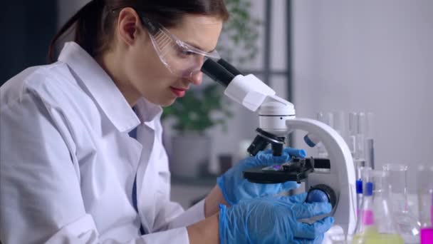 Recherche sur l'ADN dans un laboratoire moderne, la femme regarde l'échantillon au microscope — Video