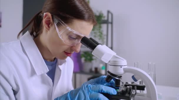 Jovem cientista está examinando amostras ao microscópio — Vídeo de Stock