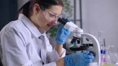 Araştırmalar için biyolojik laboratuvar, kadın mikroskop altında örnekleri inceliyor.