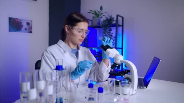 Virólogo está examinando la muestra bajo el microscopio, trabajando en el laboratorio de ciencias — Vídeo de stock