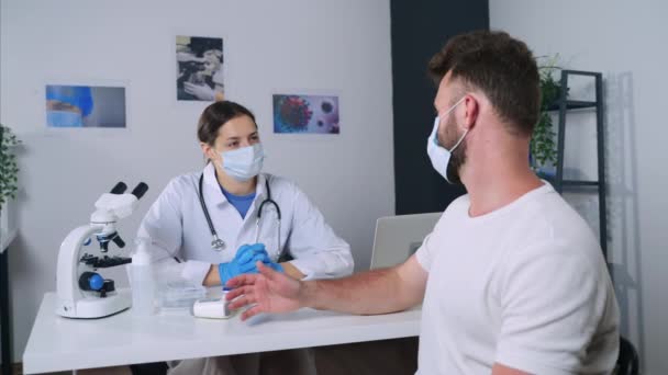 Paciente está consultando com o médico na clínica médica, ambos estão usando máscara facial — Vídeo de Stock