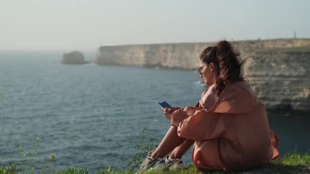 Fiatal nő pihentető telefon a tenger mellett — Stock videók