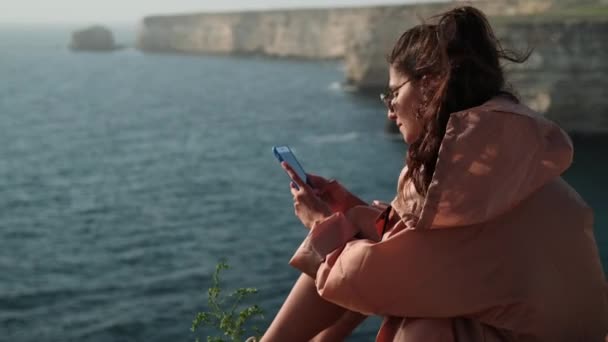 Donna sta comunicando tramite chat online in smartphone, seduto sulla riva del mare aperto — Video Stock