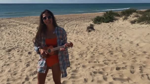 Беззаботная смеющаяся женщина играет на укулеле на пляже — стоковое видео