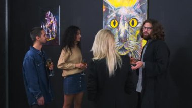 Modern sanat sergisinin konukları resim izliyor ve rehber veya sanatçı dinliyorlar.