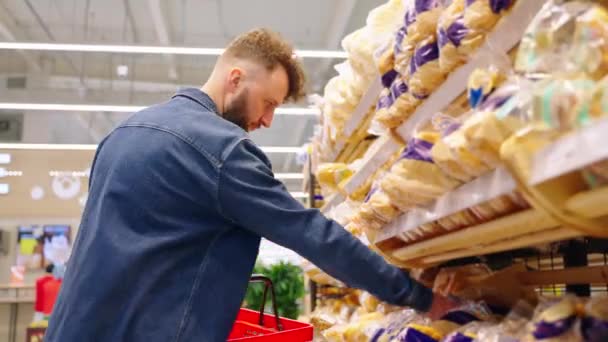 Adult man is choosing bread in supermarket, taking packed loaf gluten free — Stock Video