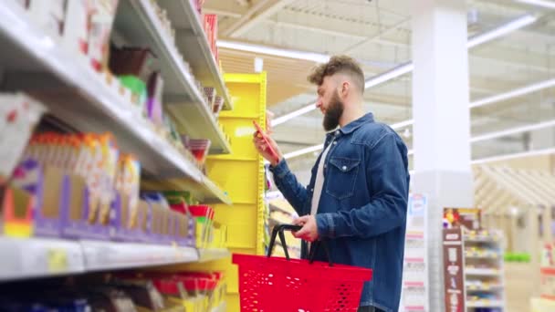 Departamento de dulces en el supermercado, el hombre está eligiendo el chocolate, lectura de etiquetas — Vídeos de Stock