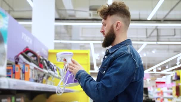 Comprador masculino está eligiendo la ropa de vapor en la tienda de electrodomésticos — Vídeos de Stock