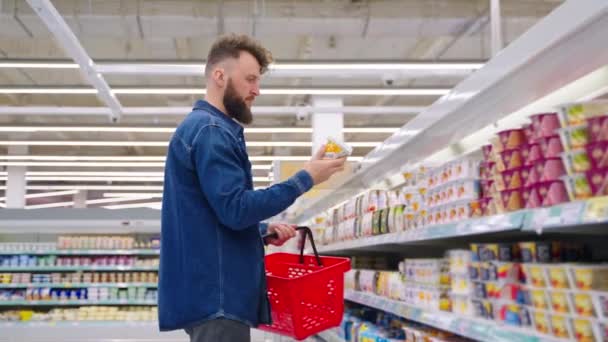 L'uomo sta facendo la spesa al supermercato, scegliendo yogurt a basso contenuto calorico — Video Stock