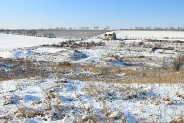 Karda bir köy, bir tarla ve ağaçların olduğu kış manzarası.