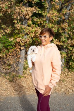 Sonbaharda dışarıda yürürken küçük bir köpeğe sarılmış mutlu bir son sınıf öğrencisi.