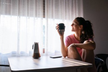 Sabahın erken saatlerinde pencerenin kenarında kahve içen genç bir kadın.