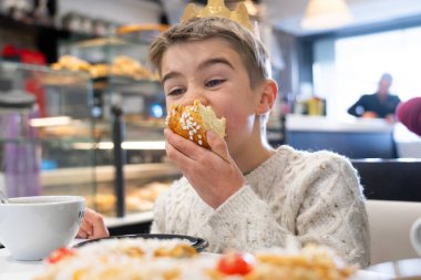 Kafede tezahürü Roscon de Reyes ile kutlayan kağıt taç takan mutlu çocuk.