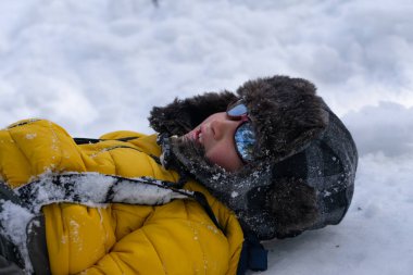 Kışlık giysiler ve güneş gözlüğü takan genç çocuk taze karda uzanmanın keyfini çıkarıyor.