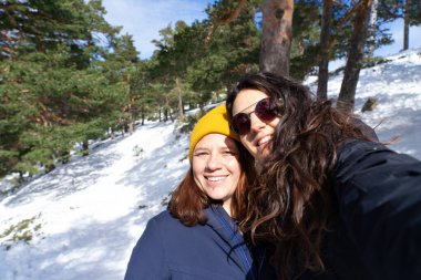 Karlı bir dağ ormanında selfie çeken iki kadın yürüyüşçü kış manzarasının tadını çıkarıyorlar.