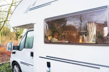 Dizüstü bilgisayar kullanan bir kadın, park halindeki bir karavanda çalışıyor.