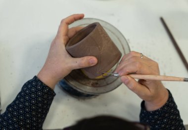 Sanatçı elleri özenle dekoratif desenleri çömlek çarkına işlenmemiş kilden bir kaba oyuyor.