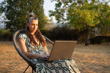 Bahçedeki sandalyede otururken dizüstü bilgisayar kullanan gri saçlı kadın.