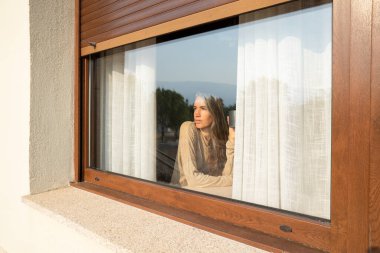 Pencereden dışarı bakıp hayatı düşünürken elinde kahve fincanı tutan düşünceli bir kadın.