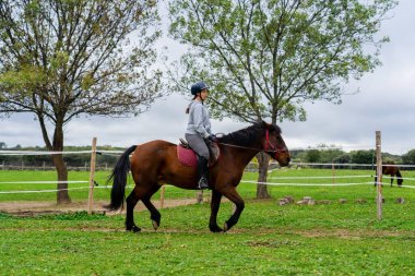 Kırsal kesimde binicilik eğitimi sırasında ata binen genç bir kadın.