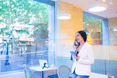 Akıllı telefondan iletişim kuran, elinde tablet tutan, kahve dükkanından iş yöneten profesyonel bir kadın.