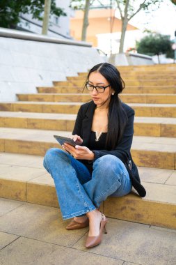 Tablet üzerinde uzaktan çalışan genç bir kadın şehir basamaklarında oturuyor.