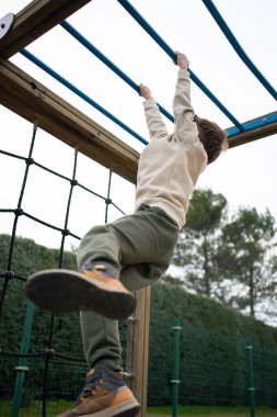 Çocuk oyun parkında maymun parmaklıklarına tırmanıyor. Güç, zindelik ve çocukluk sevinci gösteriyor.