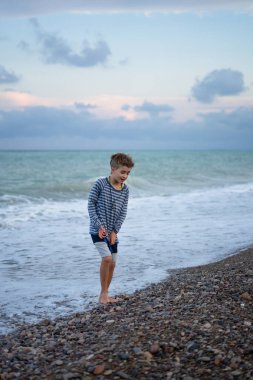 Çocuk sahilde huzurlu bir yürüyüşün tadını çıkarırken dalgalar yavaşça ayaklarını kaplıyor.